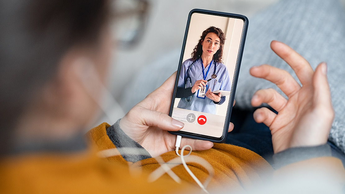Frau nutzt Videosprechstunde via Smartphone mit Kopfhörer